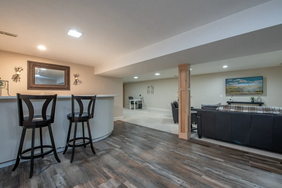 A warm, open space featuring a bar area with stools, seating area with a couch, framed mirror, and decorative wall art. The area feels social and welcoming—ideal for gatherings and celebrations after a day out.