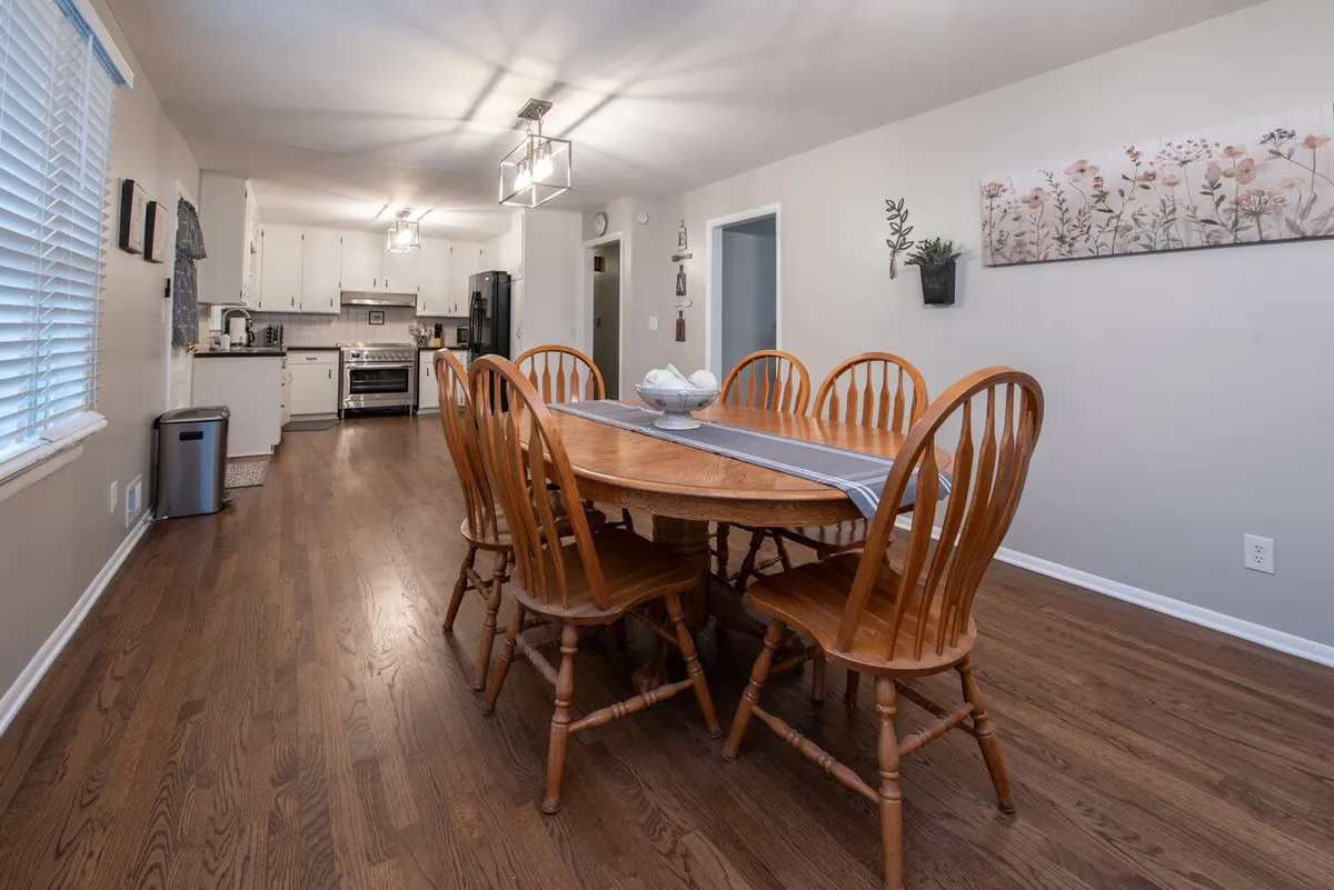 A dining space with a large table set under chandelier lighting, with a view into the kitchen entrance and decorative wall art. The warm lighting and inviting setup create an ideal spot for intimate meals, celebrations, or morning coffee moments.