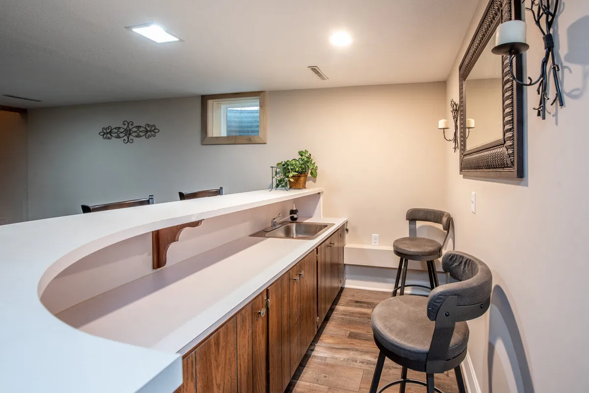 A casual, welcoming bar area with curved countertop, bar stools, a decorative mirror, and touches of greenery. The bright, airy atmosphere is perfect for gathering with friends, sharing a drink, or preparing for a stroll into town. The setup invites easy conversation and socializing, blending home comfort with the spirit of friendly neighborhood gatherings.