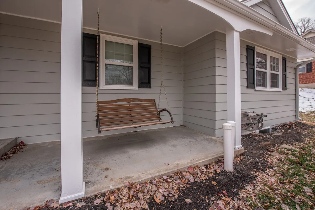 A charming front porch with a swing bench and shuttered windows, inviting guests to relax and share stories in a serene outdoor extension of the living space.