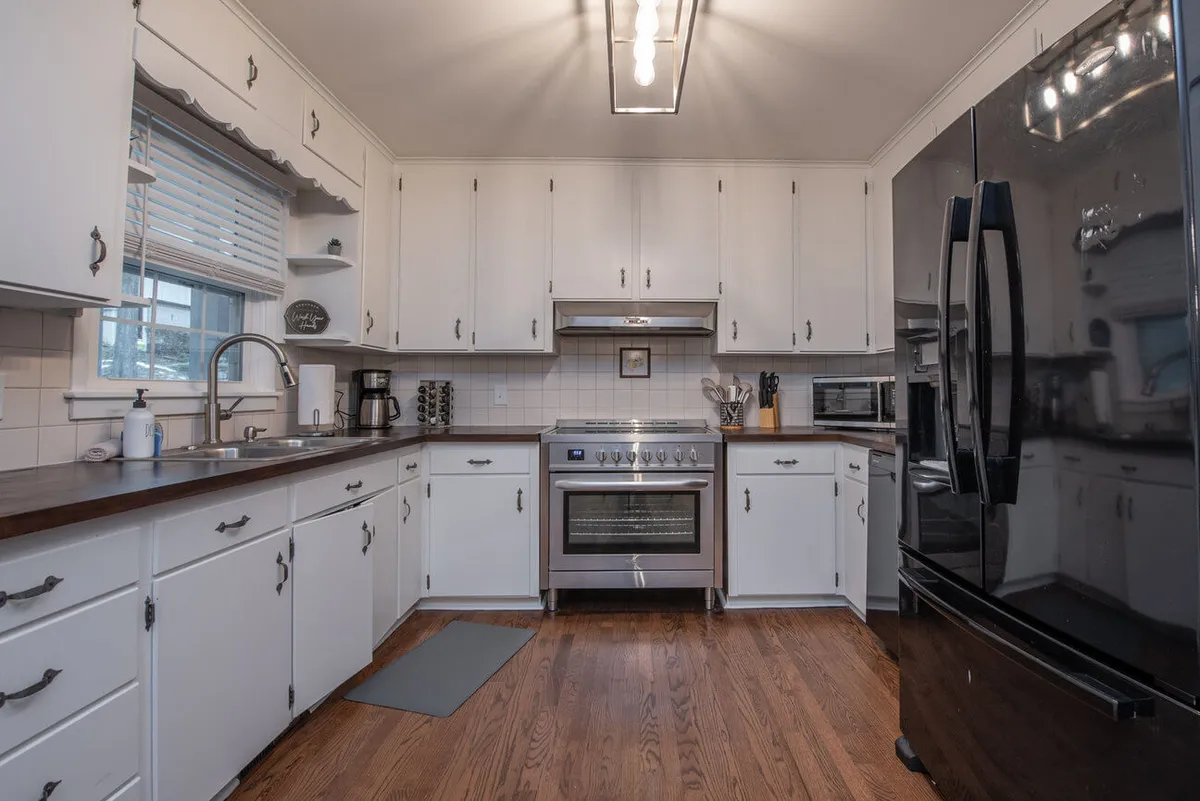 This image showcases a well-equipped kitchen with stainless steel appliances, a dark countertop, white cabinetry, and a black refrigerator, all bathed in a warm and welcoming atmosphere. The layout offers ample workspace and storage, making the space ideal for cooking, baking, and gathering as a family.